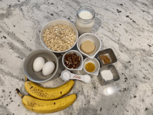 bananas, eggs, tablespoon, and oats on a marble countertop to show ingredients needed to make recipe
