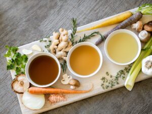 Cutting board with 3 soup bowls surrounded by carrots, celery, mushrooms, and garlic.