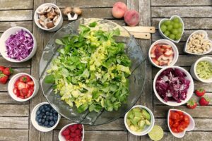 bowl of lettuce with surrounding bowls of fixings for salad like blueberries, strawberries, grapes, mushrooms, avocado, and tomatoes