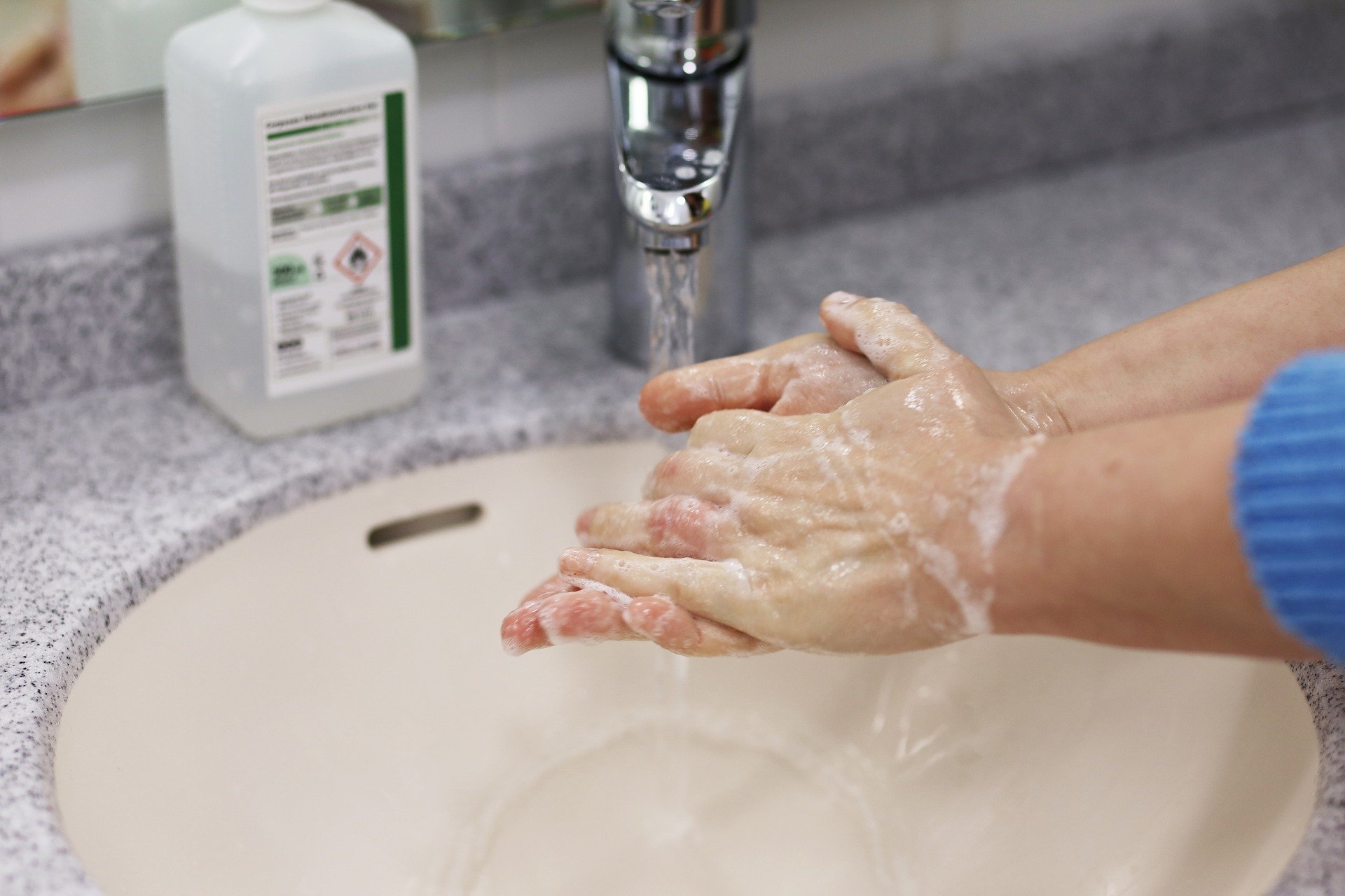 Two hands lathering soap under faucet.