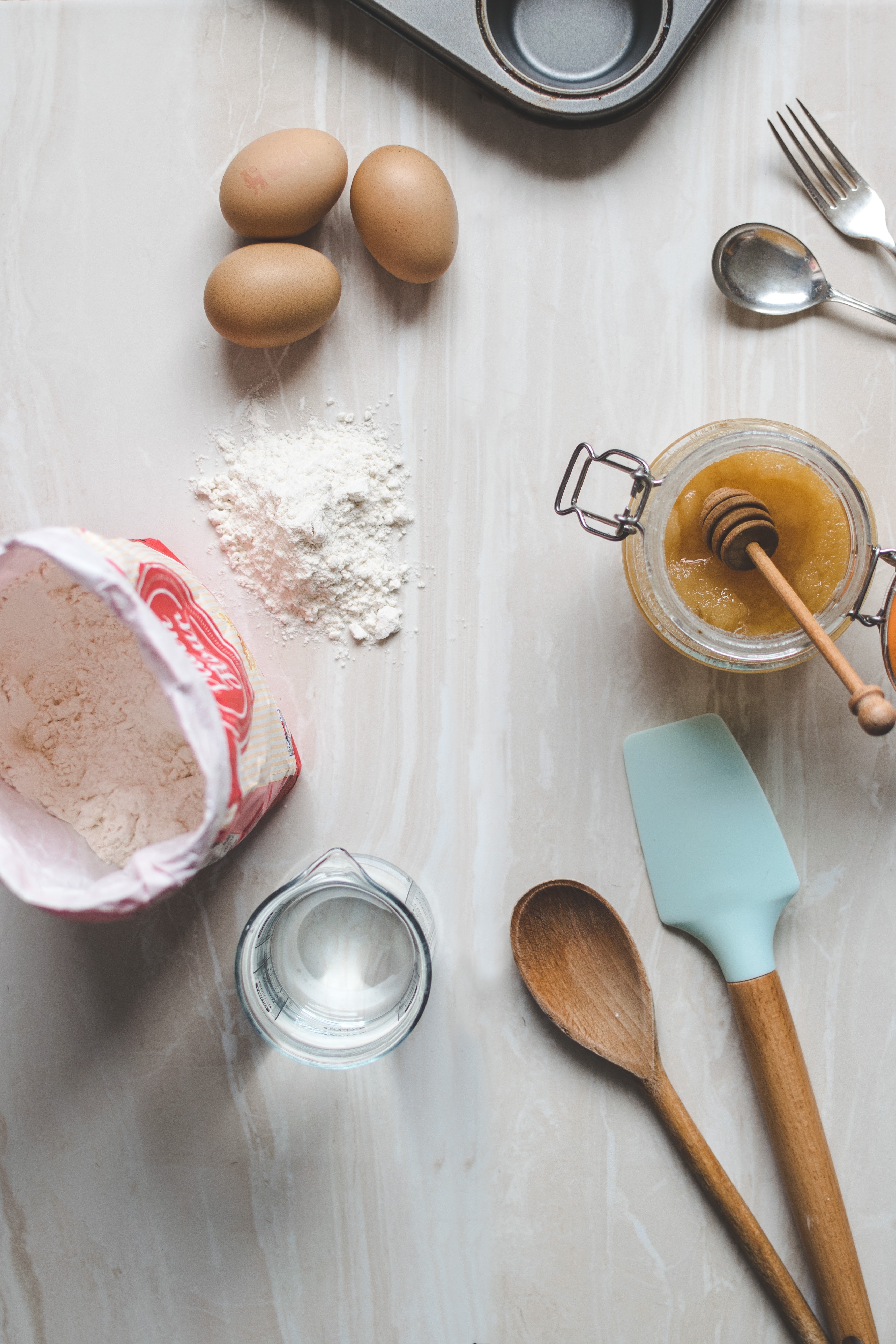 spatulas, flour, eggs, water, pan, and spoon and fork on counter