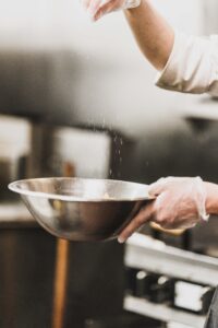 Gloved hands sprinkling spices in bowl.