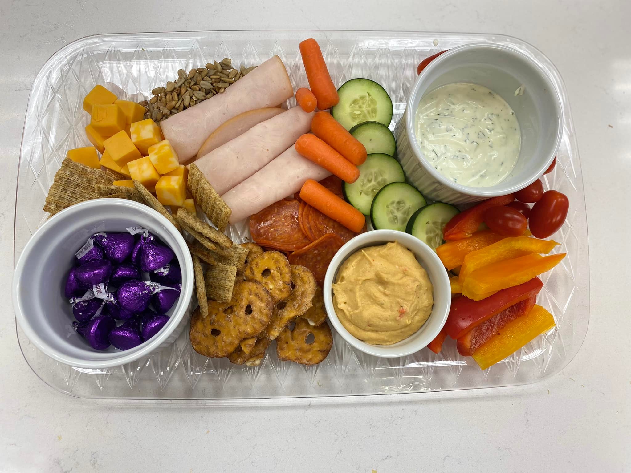 Charcuterie Board. Board with various foods including pretzels, hummus, homeade ranch, turkey, cheese, carrots, cucumbers, and sunflower seeds.