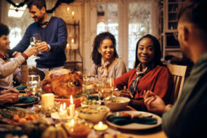 Happy African American woman and her friends communicating while celebrating Thanksgiving at dining table.