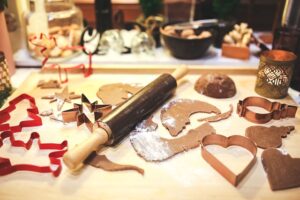 Cookie cutters, with raw cookie dough and flour on top of a counter with a rolling pin.