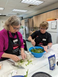 2 food volunteers mix together ingredients for the salad