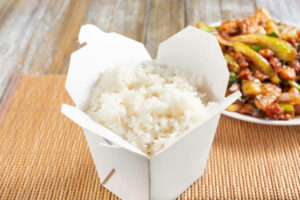 A view of a Chinese take out container full of white steamed rice, in a restaurant or kitchen setting.