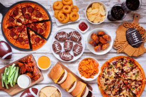 Super Bowl or football theme food table scene. Pizza, hamburgers, wings, snacks and sides. Above view on a white wood background.