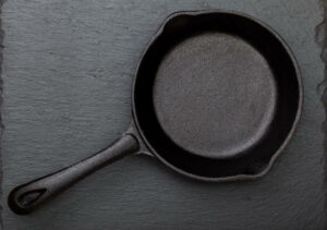 Empty cast-iron frying pan on a black slate background (top view)