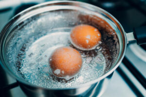 Saucepan stainless steel with boiling eggs breakfast in a water on a gas stove top view.
