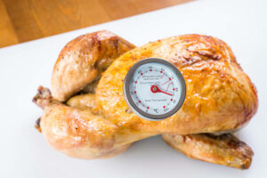 Meat thermometer and cooked roast chicken at the correct internal temperature.