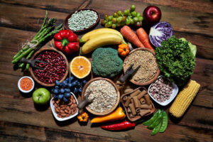 Dietary and healthy food themes. Table top view of fresh vegetables and legumes on rustic wooden table. Food is rich of fiber ideal for dieting and healthy eating. Includes corn, avocado, broccoli, orange fruit, grapes, bell pepper, lettuce, banana, apple almonds and wholegrain pasta.