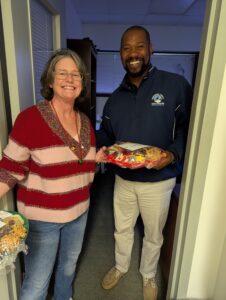 A woman delivers Christmas cookies to a man in an office.