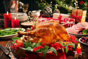 Christmas turkey dinner. Baked turkey garnished with red berries and sage leaves in front of Christmas tree and burning candles