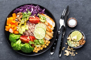 Buddha bowl dish with chicken fillet, brown rice, avocado, pepper, tomato, broccoli, red cabbage, chickpea, fresh lettuce salad, pine nuts and walnuts. Healthy balanced eating. Top view