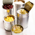 Different kinds of vegetables in cans on kitchen table background.