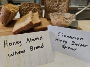 homemade honey almond wheat bread sliced up on a cutting board, with a small dish of cinnamon honey butter spread